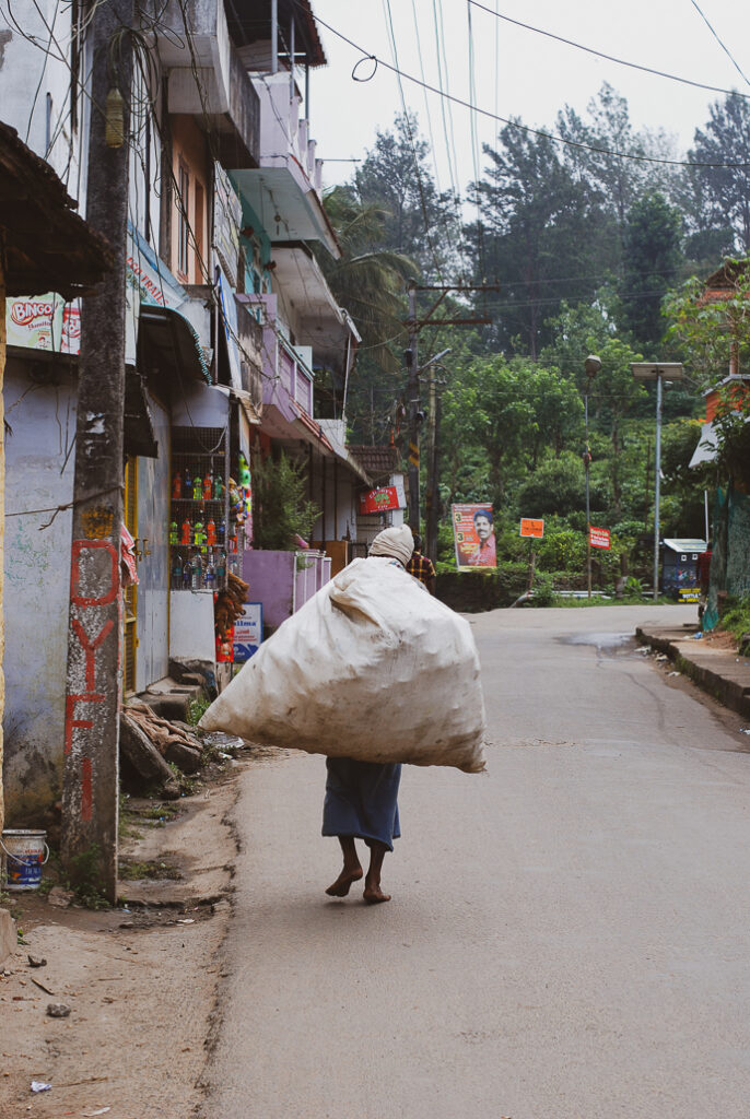 A rag picker in India walks away on a street in Thekaddy, Periyar, Kerala, India. The street is lined with shops and residences. Street and travel and Indian photography. Original photographs taken by Yuvan Kumar.