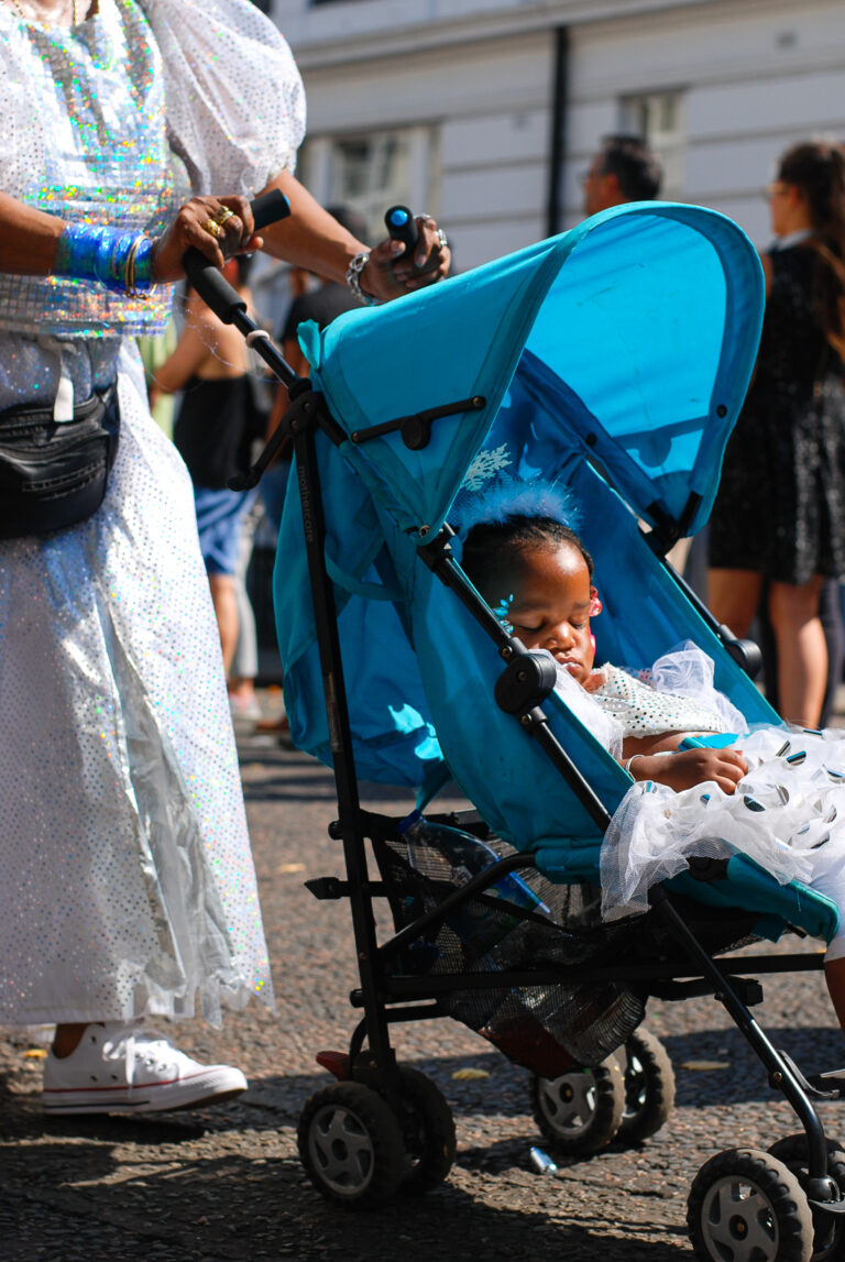 A street photograph of a child in a bright blue pram at the Notting Hill Carnival, London.